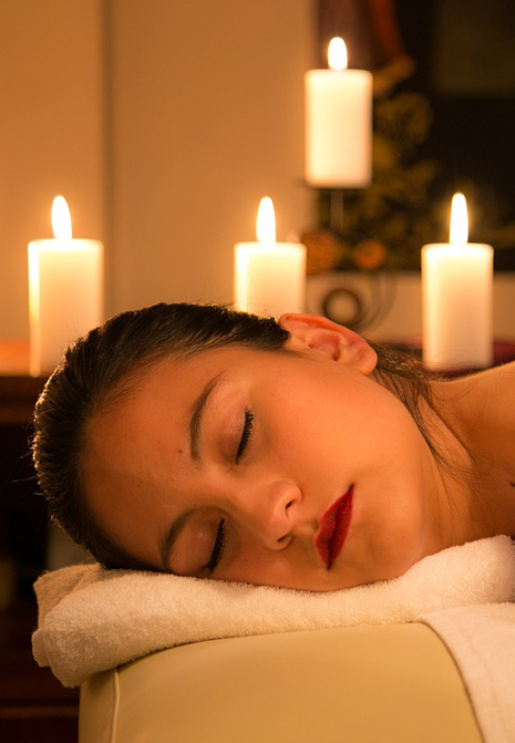 Massage érotique - Une femme est allongée sur une table de massage la tete tounée sur le côté et des bougies allumées sont en arrière plan.