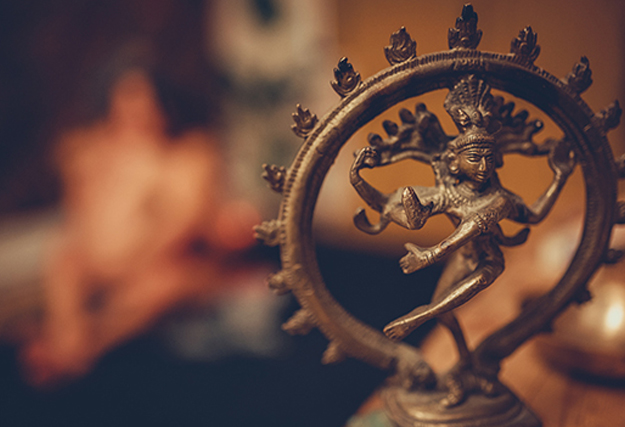 Statue de danseur hindou en bronze avec une personne floue en arrière-plan lors d'un massage tantrique